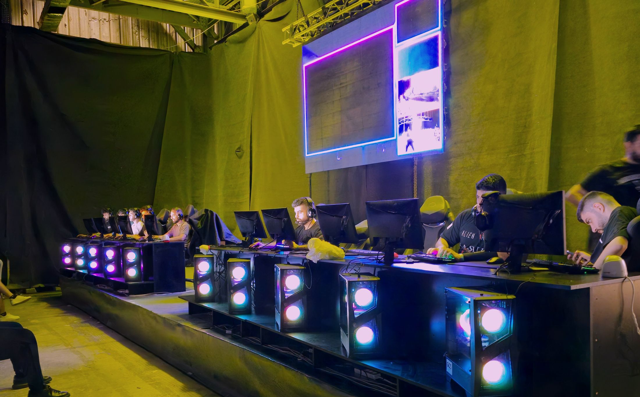 Competitive gaming event floor with players at illuminated stations in front of a large LED wall