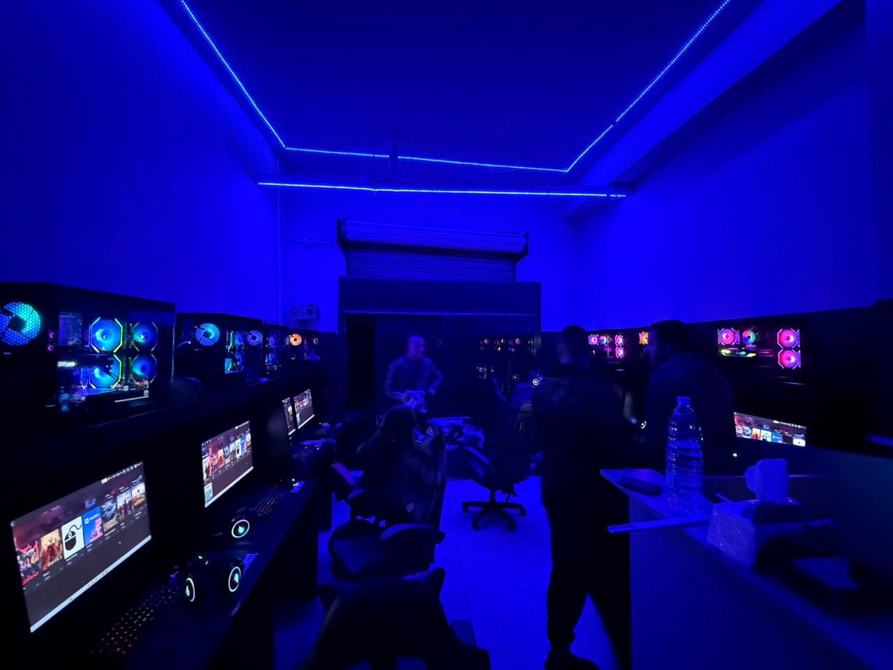 Gaming lounge on opening night, customers standing between two rows of illuminated stations under blue ceiling lighting