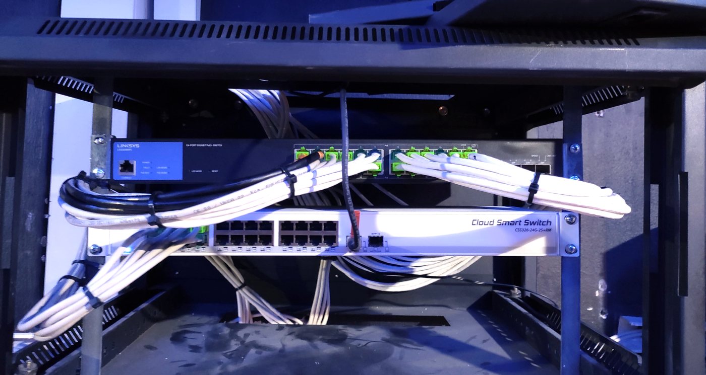 Network cabinet with a MikroTik Cloud Smart Switch and Linksys PoE switch, patch leads dressed and tied